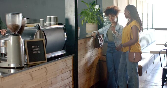 African American women friends leaning on counter pointing while waiting as barista hand appearing