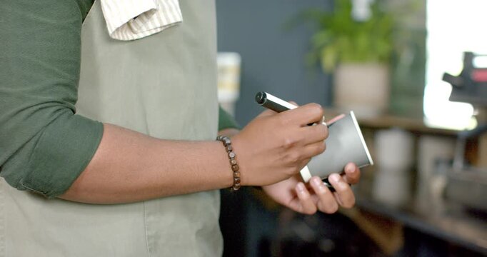 Barista is rotating gray cup, aiming marker and drawing initial at coffee counter to label drink