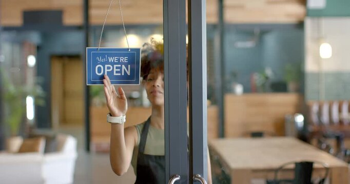 Cafe worker is reaching up, flipping closed sign to open and pulling door to welcome customers