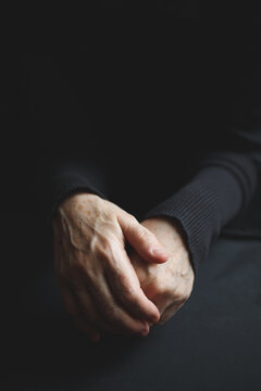 Folded senior hands against a dark background, symbolizing aging and medical care.