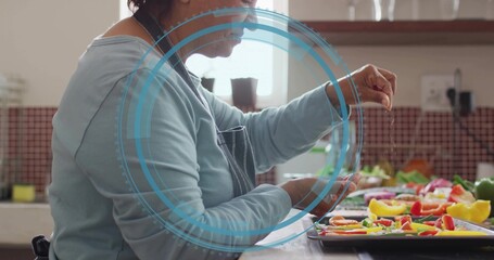 Sprinkling Indian cook in dark-apron at counter salting pepper tray with blue overlay, copy space © vectorfusionart