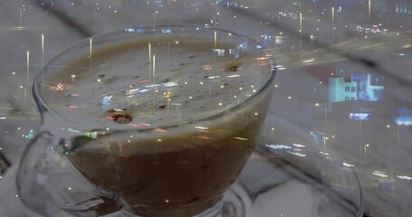 Displaying glass cup with handle holding frothy coffee on saucer in cafe, spoon, city lights