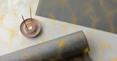 Naklejka premium Showing rolled gray yoga mat unrolling on stone floor, with flat mat and incense holder