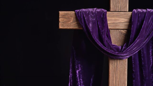 A wooden Christian cross draped with a rich purple cloth against a dark, somber background, symbolizing Lent or mourning.