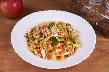 A ready-made salad of cabbage, carrots and apples with nuts and sauce on a white plate on a wooden table.