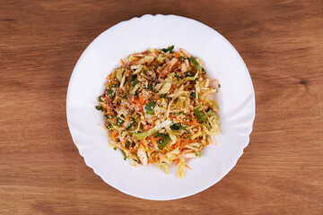 A ready-made salad of cabbage, carrots and apples with nuts and sauce on a white plate on a wooden table.