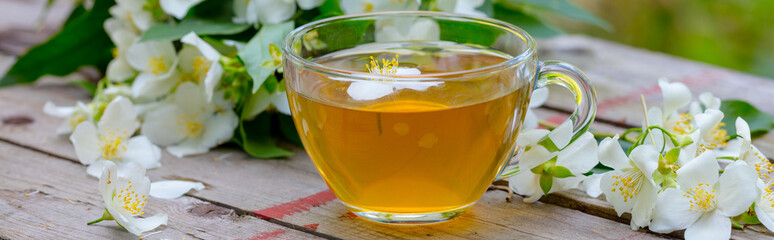 Fototapeta premium A cup of green tea with jasmine flowers on grunge wooden table outdoors
