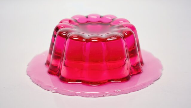 Colorful pink jelly dessert in a vintage mold, placed on a white surface. Soft light highlights the transparent texture and glossy finish of the gelatin.