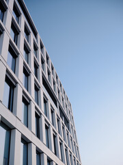 Fototapeta premium Low angle view of a modern office building exterior with glass windows and geometric facade, leaving large copy space in a clear blue sky for corporate and business background use.