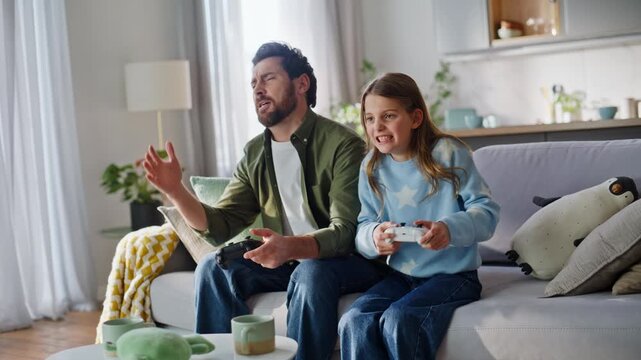 Father child playing video game sitting home sofa. Excited teenager girl win 