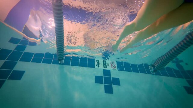 Female swimmer pushing off pool wall underwater in indoor lap pool