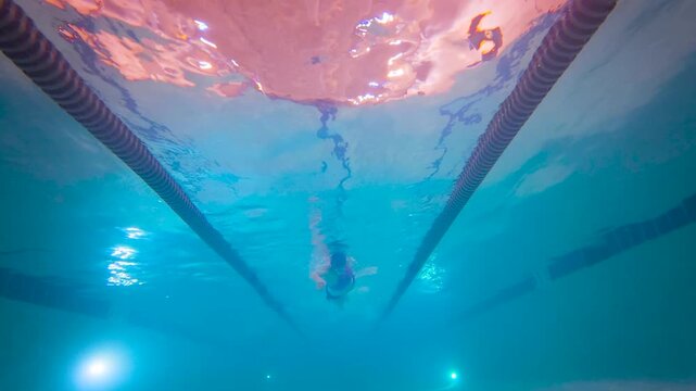 Female swimmer freestyle underwater passing overhead in indoor pool