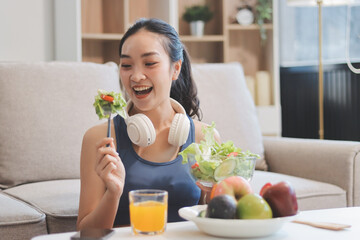 Fit young Asian women in activewear sitting on yoga mat and eating fresh vegetable salad after workout, representing clean eating, fitness lifestyle, wellness routine and health balance.