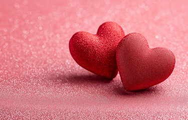 Fototapeta premium two red hearts on a pink glittery background with copy space for a valentine's day celebration, a love concept. 