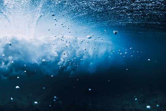 Underwater view of breaking ocean wave, clear water with sun light rays and bubbles