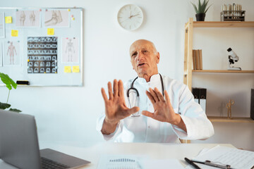 senior male doctor wearing white coat work on laptop in hospital clinic, say no thank you with...