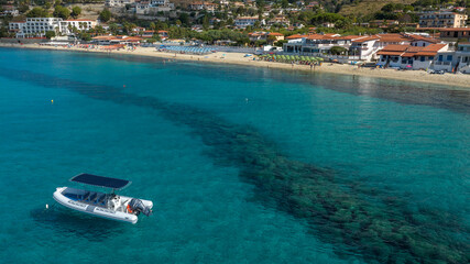 Aerial view of a peaceful Mediterranean bay. A white RIB boat is anchored on transparent turquoise water. In the background, it's the sandy beach of Santa Maria di Ricadi,in Calabria, southern Italy. © Stefano Tammaro