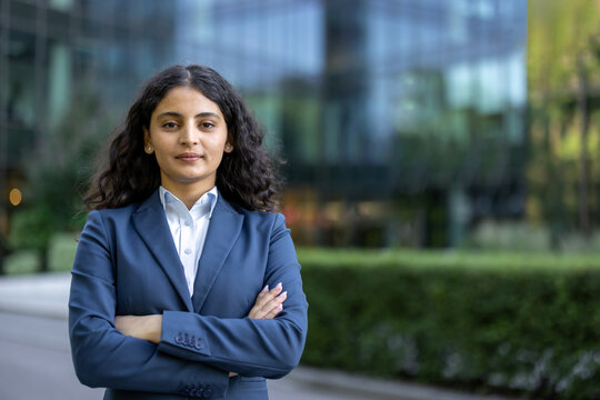 Confident indian businesswoman in a tailored blue suit stands outdoors in a city, arms crossed, looking determined professional executive portrait conveying leadership and ambition
