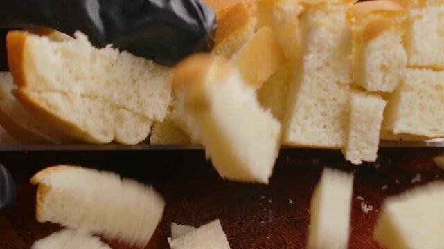 A hand scoops up a pile of freshly diced bread cubes from a wooden cutting board. The cubes are ready to be toasted into crispy, golden homemade croutons for soups or salads