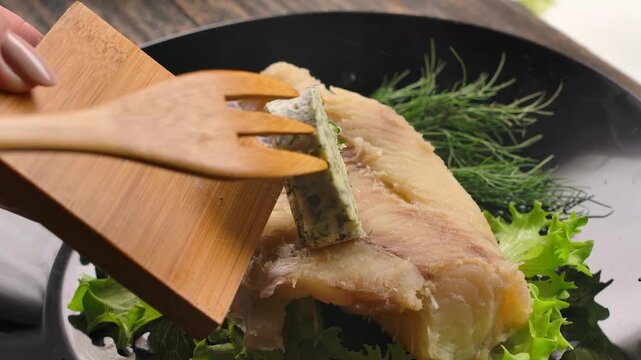 Close-up of a slice of garlic dill butter melting on a hot, flaky cod fillet. Perfect footage for seafood recipes, healthy eating concepts, and gourmet cooking content