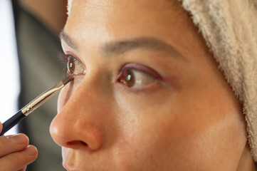 Woman blending eyeshadow with a makeup brush on her face.
Beauty and skincare routine concept. Professional makeup application, cosmetics, self-care, and personal grooming. Close-up portrait.