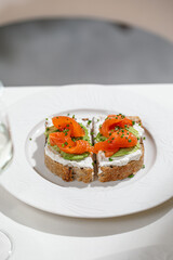 Toast with smoked salmon sliced avocado and cream cheese topped with fresh chives on white plate
