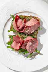 Toast topped with sliced cured beef fresh greens and grated cheese served on elegant white plate