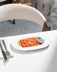 Fresh salmon slices served with creamy sauce fresh herbs and olive oil on elegant white plate