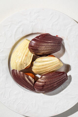 Assorted chocolate madeleine cakes with glossy finish served on white plate in elegant light