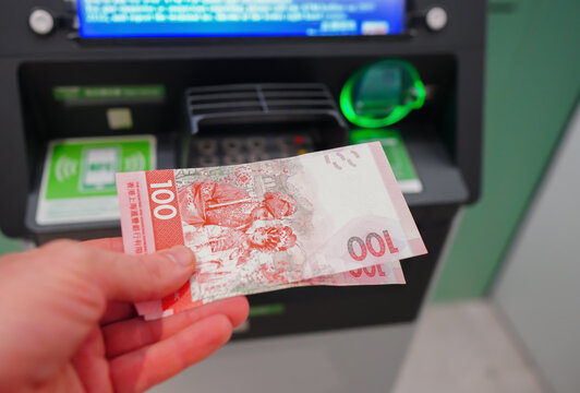 Hundred Hong Kong dollars bill in hand from ATM. Withdrawing cash from ATM HK. Person holding red hundred Hong Kong dollars bill in front of ATM. Withdraw Money from ATM. Currency exchange service