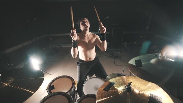 Energetic shirtless drummer playing drums during concert
