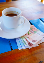 Coffee cup on table with yuan bill money in cafe. Payment coffee drink on breakfast. Yuan biill money on table cafe as tip. Coffee cup with yuan bill as payment, tip in China. Restaurant tips tea.