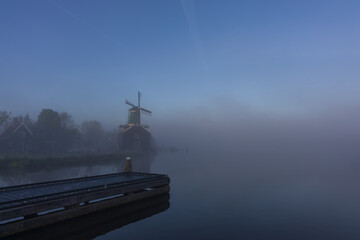 Historic green windmill and wooden pier in thick morning mist at Zaanse Schans
