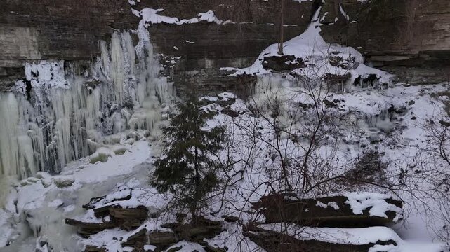 Pull drone shot of frozen river, rock bluff and icicles.