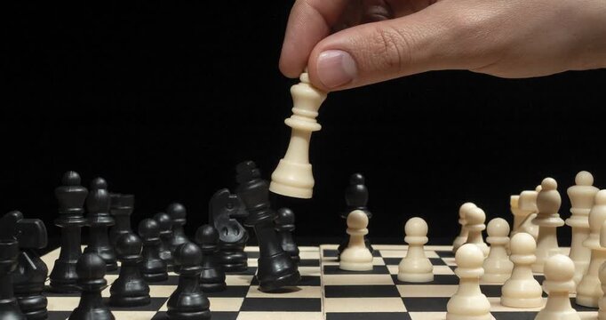 A zoom out of a male hand doing a checkmate to the black pieces on a chess board
