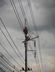 Electrical lineman worker team replacing high voltage suspension insulators on concrete pole using hot stick method for live line maintenance without power outage.