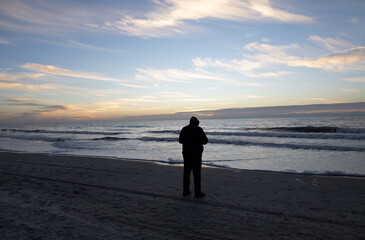 Silhouette of a Person Standing on the Beach at Sunrise with Ocean Waves and Dramatic Cloudy Sky