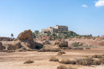 Saddam Hussein Palace stands prominently on a hill, overlooking the arid landscape dotted with palm trees and ancient ruins.