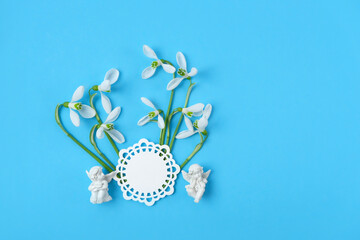 Fototapeta premium little angels figurines and white snowdrops flowers on blue background. symbol of spring season. faith in God, Christianity Feast, church holiday, Easter concept. Romantic vibes composition. flat lay
