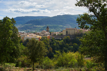 Scenic view of Privas town in the Ardeche region, France. A historic cityscape with a church tower and ancient buildings nestled among green hills and mountains.