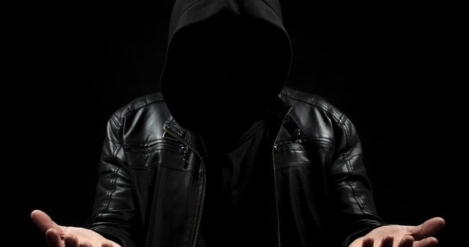 a zoom out of a faceless hooded man in the shadows ready to holding or receiving something with his boths hands