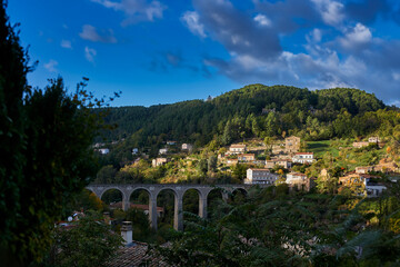 Obraz premium : Historic stone viaduct in the mountains near Privas, Ardeche. A majestic arched bridge surrounded by autumn-toned forests and traditional French countryside houses.