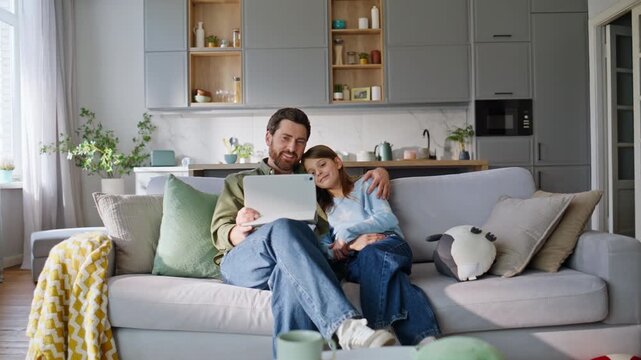 Bonding father daughter browsing tablet sitting home sofa. Happy dad girl