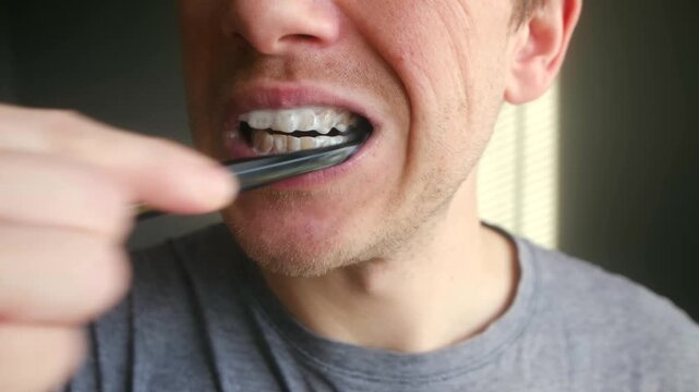 Close up man meticulously brushing his teeth with black toothbrush, whitening charcoal toothpaste part of his daily morning dental hygiene, oral care routine. Man brushing teeth with toothpaste