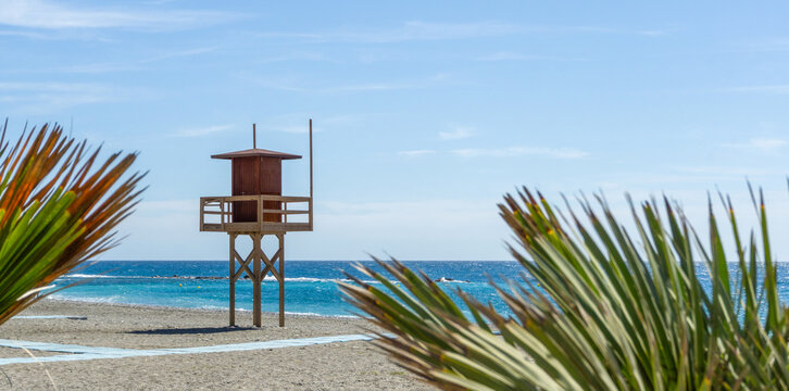 Scenic Beach View in Almunecar Costa Tropical Spain Featuring a Wooden Lifeguard Tower Framed by Palm Leaves Overlooking the Mediterranean Sea