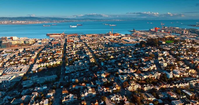 Residential neighborhoods of San Francisco on the green hilly streets. Drone flight over the cityscape at sunset. Bay waterscape with ship on roadstead at backdrop.