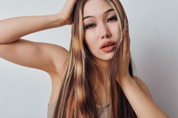 Obraz premium Woman with long light brown hair posing with hand on forehead and cheek, looking at camera with neutral expression. Studio portrait with natural makeup and smooth skin.