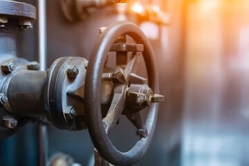 An industrial close-up of a valve wheel, hinting at engineering and industry. The sun casts a warm glow on the metallic surface, enhancing texture and shadows