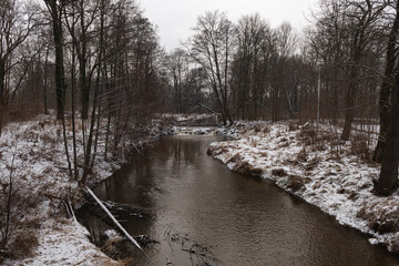 Wodospad na niewielkiej rzece. Jest zima. Brzegi pokryte są warstwą śniegu. Rzekę miejscami pokrywa lód. Wzburzona woda na wodospadzie przepływa pomiędzy lodowymi czapami. © boguslavus