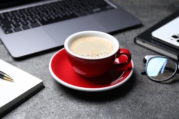 Naklejka premium Cup of aromatic coffee, laptop and office essentials on grey table, closeup